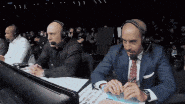 two men wearing headphones are sitting in front of a computer monitor
