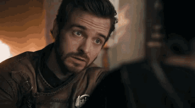 a man with a beard is wearing a brown leather jacket and looking at something