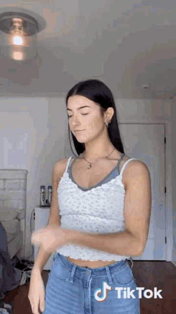a girl in a white tank top and blue jeans is dancing in a room .
