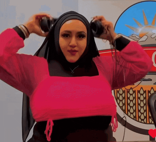 a woman wearing a hijab and a pink top is holding a pair of headphones