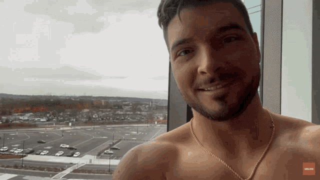 a man without a shirt is smiling in front of a window with a red arrow pointing to the left