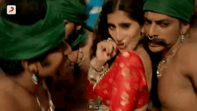a woman in a red saree is surrounded by a group of men in green turbans .