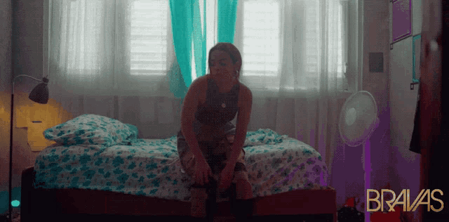 a woman sits on a bed with bravas written on the bottom right