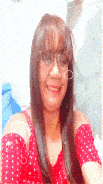 a woman wearing glasses and a red off the shoulder top smiles for the camera