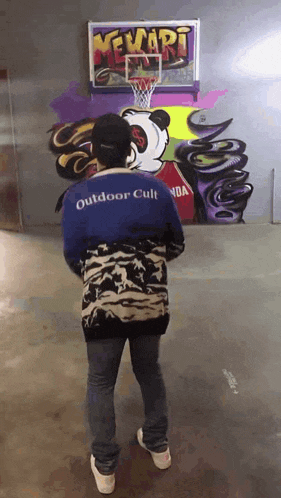 a person wearing a blue outdoor cult shirt is standing in front of a basketball hoop .