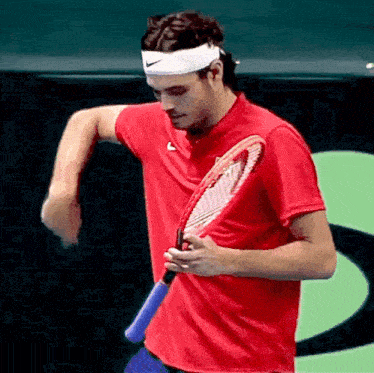 a man in a red shirt holds a tennis racket
