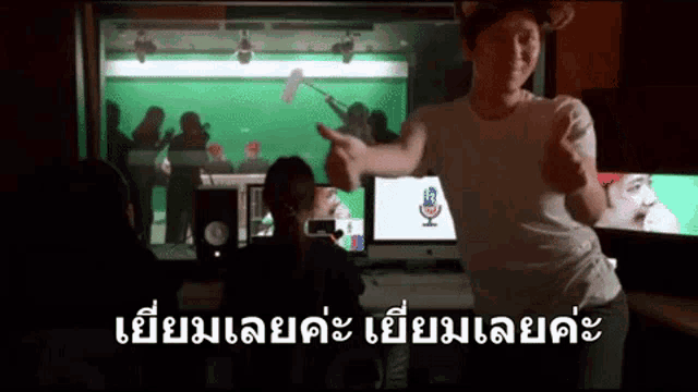 a man in a white shirt is giving a thumbs up in front of a green screen in a recording studio .