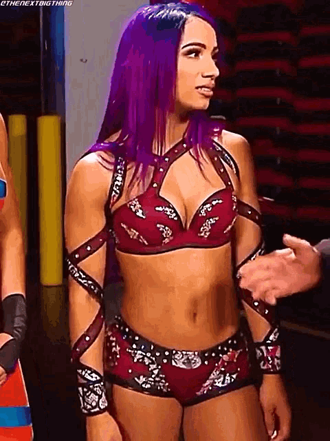 a woman with purple hair is standing next to a man in a red bra and shorts .