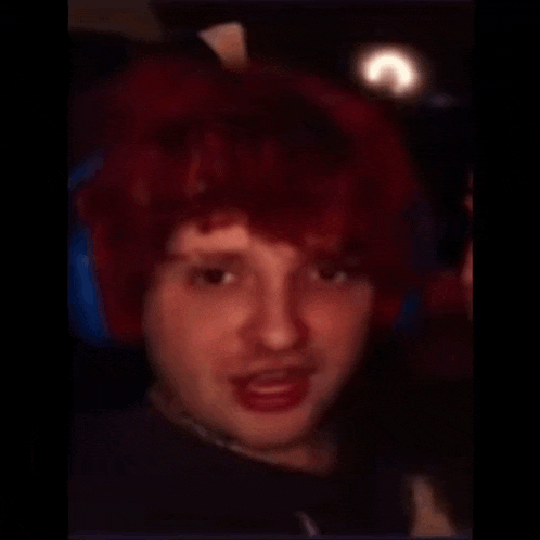 a man with a shaved head and red hair looks at the camera
