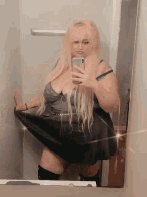 a woman is taking a selfie in a bathroom mirror .