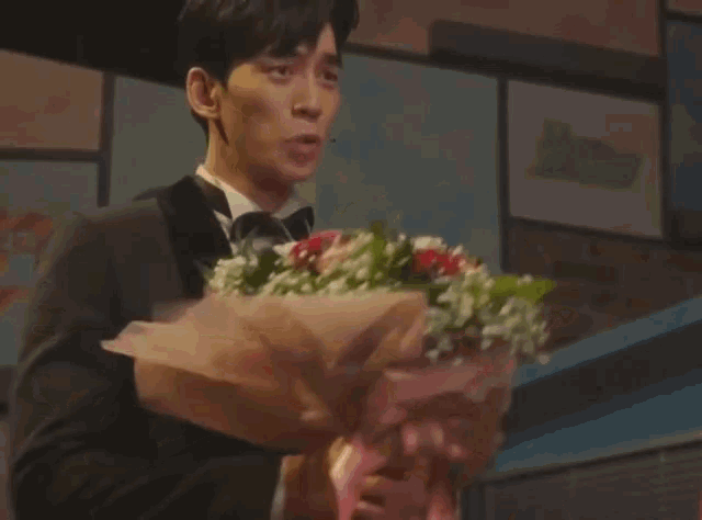 a man in a tuxedo holds a large bouquet of flowers