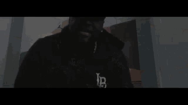 two men are standing next to each other in a dark room . one of the men is wearing a hoodie .