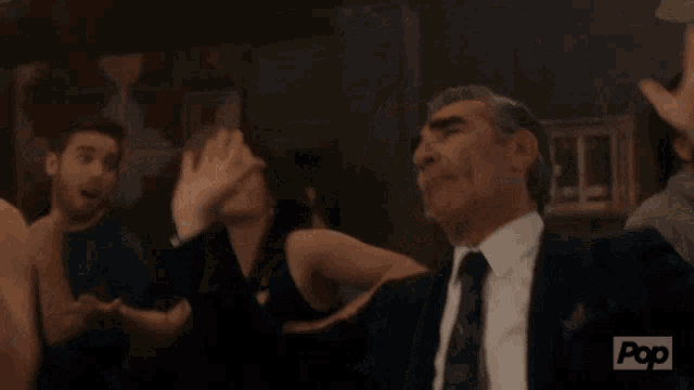a man in a suit and tie is raising his hands in the air with a pop logo in the corner