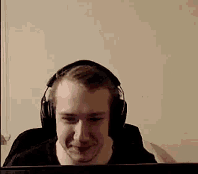 a man wearing headphones is smiling while looking at a laptop screen .