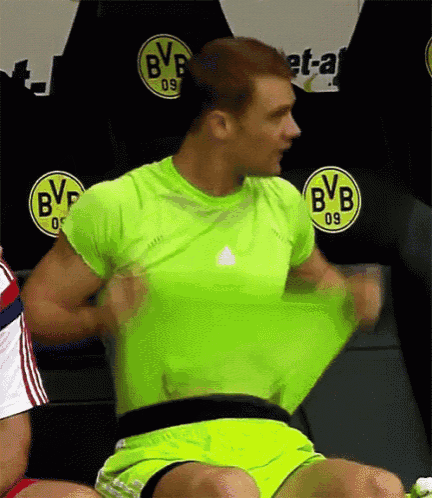 a man in a green shirt and yellow shorts is taking off his shirt in front of a bvb logo .