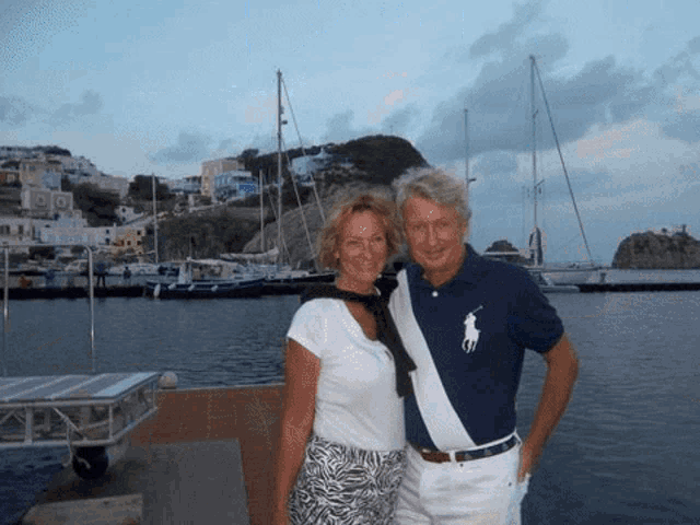 a man and woman posing for a picture in front of a harbor