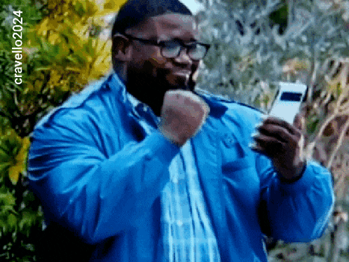 a man wearing glasses and a blue jacket is holding a cell phone in his hand