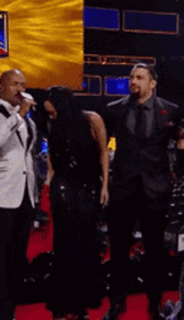 a man in a tuxedo is singing into a microphone while a woman stands behind him