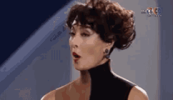 a woman with short hair is wearing a black turtleneck and earrings and making a funny face .