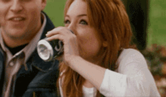 a woman is drinking from a can while sitting next to a man .