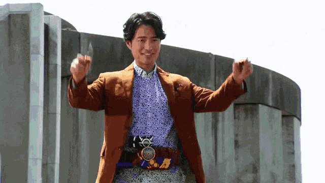 a man wearing a brown jacket and a purple shirt is standing in front of a building with his arms outstretched