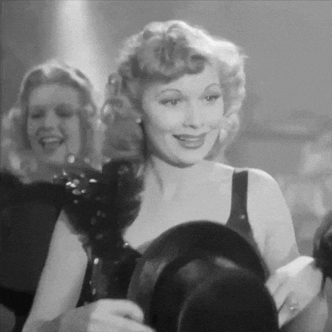 a black and white photo of a woman holding a top hat in a room .