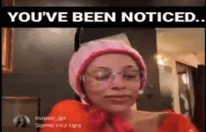 a woman wearing a pink hat and glasses says `` you 've been noticed '' in a video .