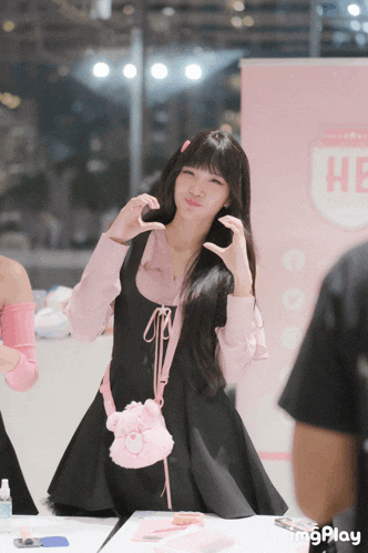 a girl wearing a black dress and a pink shirt stands in front of a sign that says he