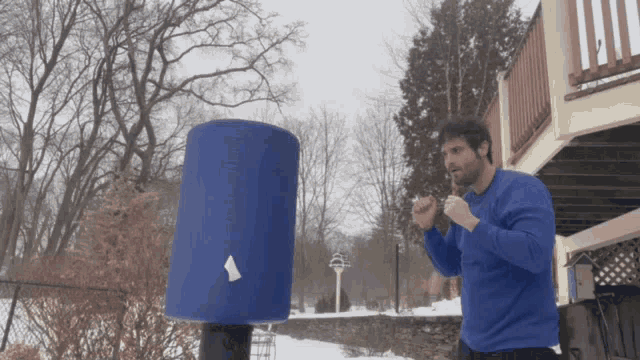 a man in a blue sweater is standing in front of a blue cylinder with a white triangle on it