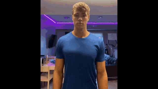 a young man wearing a blue t-shirt is standing in a living room .