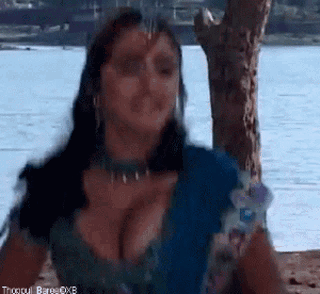 a woman is standing in front of a body of water with a tree in the background