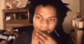 a man with dreadlocks is wearing headphones and covering his mouth with his hands .