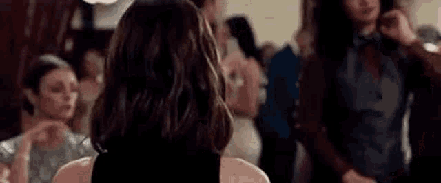 a woman in a black dress is looking over her shoulder at a crowd of people at a party .