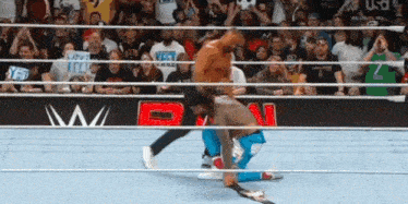 a man is kneeling down in a wrestling ring while another man is standing in the ring .