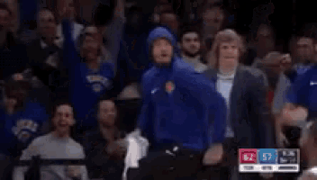 a man in a blue jacket is dancing in a crowd at a basketball game .