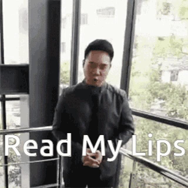a man in a suit and tie is standing in front of a window and says `` read my lips '' .