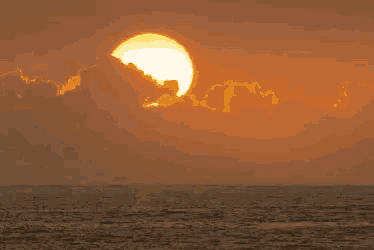 the sun is setting over the ocean with a cloudy sky in the background .