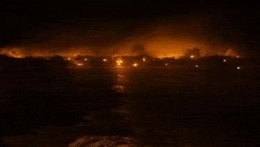 a large fire is burning in the distance over the water