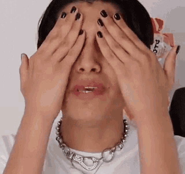 a man with black nails is covering his eyes with his hands while wearing a necklace .