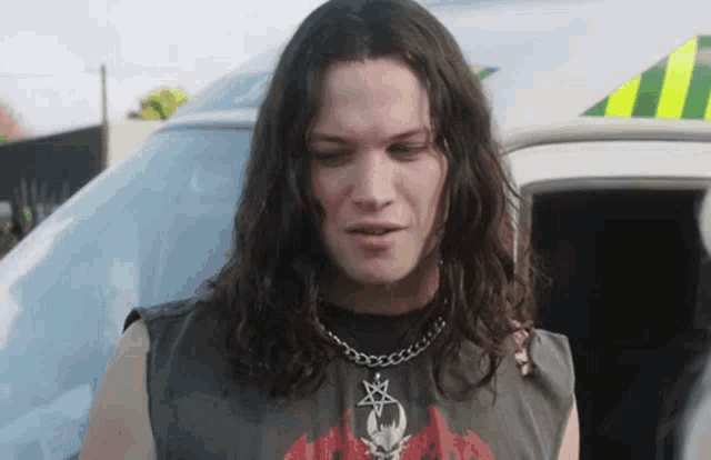 a man with long hair is standing in front of an ambulance and looking at the camera .