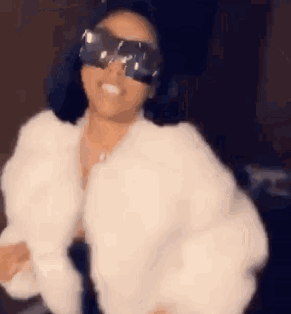 a woman in a white fur coat and sunglasses is dancing .