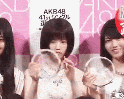three girls are holding trophies in front of a sign that says akb48 on it