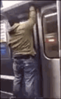 a man is getting on a subway train and holding onto the door .