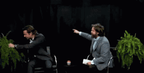 a man in a suit is sitting next to another man in a chair with a plant on his head .