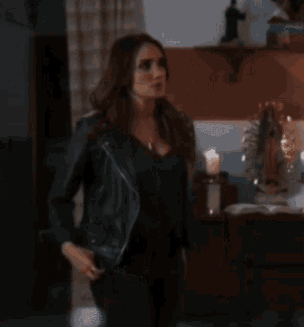 a woman wearing a black leather jacket and a black shirt is standing in a room .
