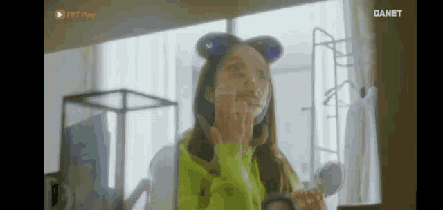 a woman in a green sweater and ears is looking at herself in the mirror .