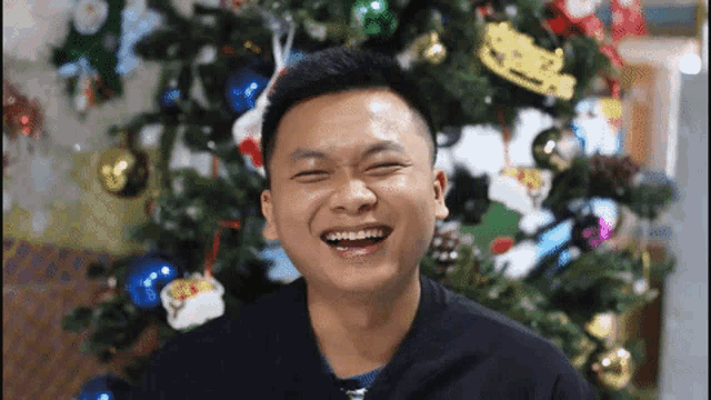 a man is laughing in front of a decorated christmas tree