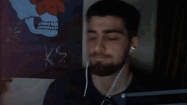 a man wearing ear buds flexes his muscles in front of a skull painting