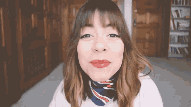 a woman with red lipstick and a scarf around her neck looks at the camera