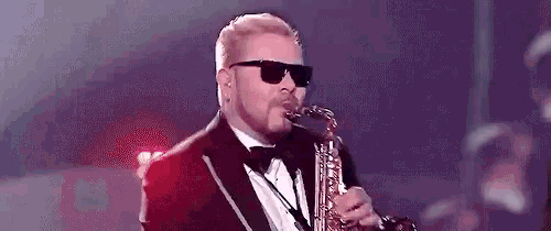 a man in a tuxedo and sunglasses is playing a saxophone on a stage .